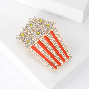 Spilla creativa a forma di popcorn con strass lucidi e smalto rosso su sfondo bianco puro