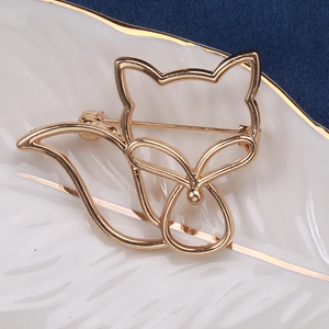 Détail d'une broche renard dorée ajourée sur plateau avec tissu bleu texturé