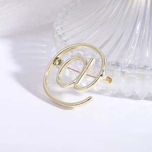 Detailed close-up of golden alloy @ symbol brooch with a metallic pin on a white surface