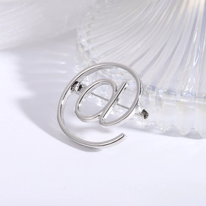 Polished silver alloy @ symbol brooch pin on minimalist white fabric background