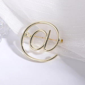 Macro detail of golden @ symbol brooch with polished finish and secure pin back
