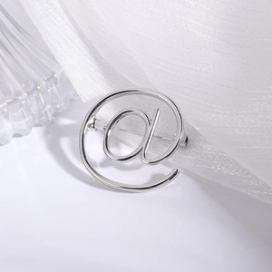 Detailed view of silver @ symbol brooch featuring a polished metal surface on silk fabric