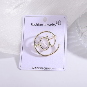 Detailed close-up of golden @ symbol brooch displayed on a lavender fashion jewelry card