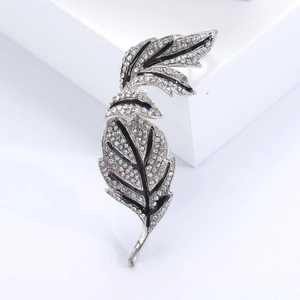 Detailed macro view of silver-toned leaf brooch featuring black enamel and white crystals
