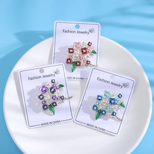 Detail of floral enamel brooches with rhinestones on a white ceramic tray with shadows