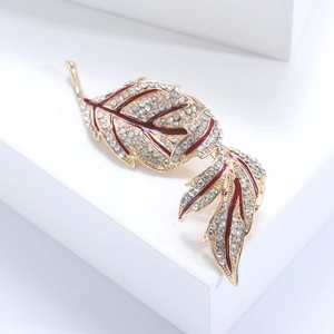 Close-up of vintage gold leaf brooch with red enamel and pavé-set sparkling crystals