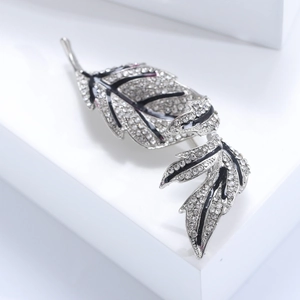 Vintage silver leaf brooch with sparkling crystals and black enamel veins on white background