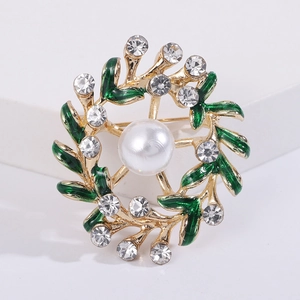 Macro detail of gold wreath brooch with green enamel leaves, white pearls and crystals