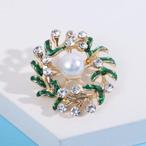Macro detail of a golden floral wreath brooch with green enamel leaves and pearls