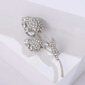 Détail d'une broche tulipe argentée avec strass étincelants sur un piédestal blanc