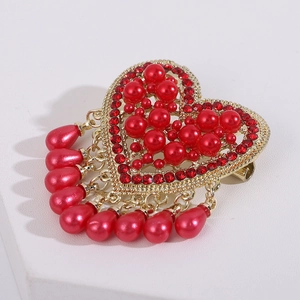 Detailed close-up of heart-shaped brooch with red pearls and golden water-drop pendants