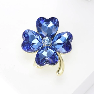 Macro view of a gold four-leaf clover brooch with deep blue crystals and heart shapes