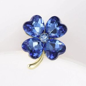 Close-up of four-leaf clover brooch with blue heart-shaped crystals and gold metal stem