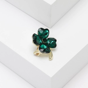 Detail of crystal four-leaf clover brooch with green heart-shaped gems and gold metal stem