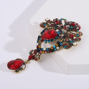 Detalle macro de broche vintage dorado con pedrería roja en forma de gota y estilo barroco