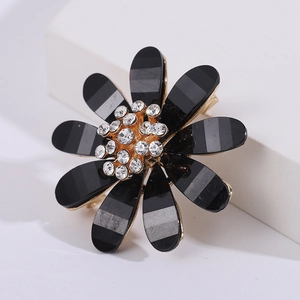 Macro detail of elegant black floral brooch with gold edges and sparkling rhinestone core