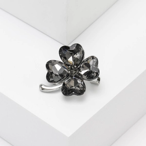 Macro detail of silver four-leaf clover brooch with dark grey heart-shaped crystals