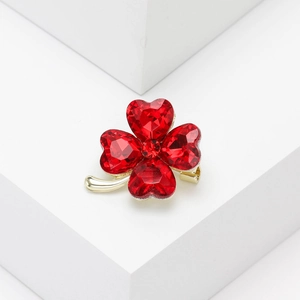 Close-up of golden four-leaf clover brooch with red heart-shaped crystals on white steps