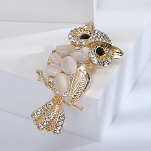 Golden owl brooch with white cat eye stones and sparkling crystals on white stand