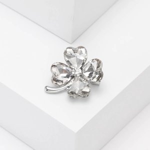 Detailed close-up of clover brooch with heart-shaped crystals on white geometric block