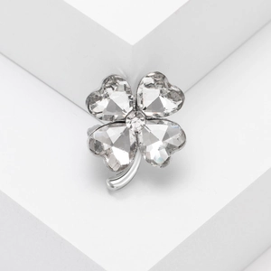 Elegant silver four-leaf clover brooch featuring heart-shaped crystals on white pedestal