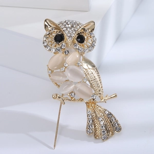 Detailed close-up of a golden owl brooch with cat-eye stones and rhinestone eyes