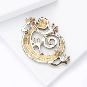 Golden lizard brooch back view with secure safety pin clasp on minimalist white pedestal