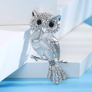 Fashion cat eye stone owl brooch with silver metal base and blue crystals on blue background