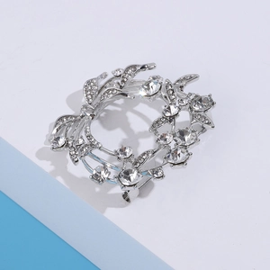 Close-up van fonkelende zilveren kransbroche met witte steentjes en gedetailleerde bladmotieven