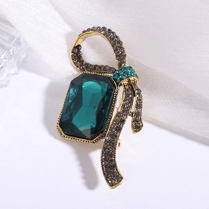 Macro detail of rectangle emerald glass brooch with crystal ribbon bow in gold finish