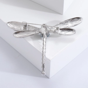 Vintage silver dragonfly brooch with blue gemstone inlay on geometric white backdrop