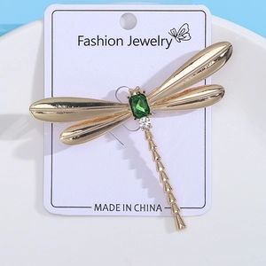 Detail view of golden dragonfly brooch with green emerald gem on jewelry card
