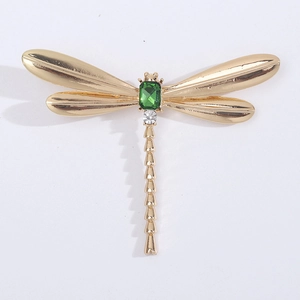 Detailed macro view of a golden dragonfly brooch featuring a central emerald gemstone