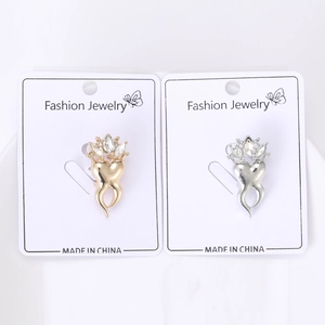 Close-up of gold and silver heart crown brooches with marquise zircons on a card