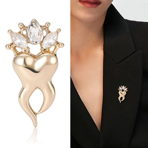 Golden crown tooth brooch with zircon stones shown on white background and black blazer