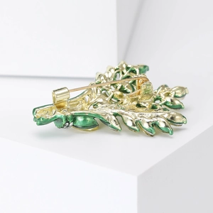 Golden leaf brooch with green enamel and pin back detail on white background