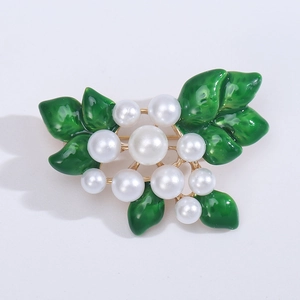 Macro view of flower brooch featuring green enamel leaves and white pearls on gold base