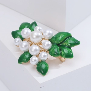 Detailed close-up of a floral pearl brooch with green enamel leaves on a white background