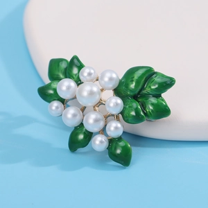 Detail of elegant gold brooch with green enamel leaves and white pearls on blue surface