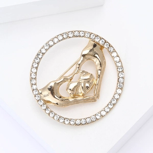 Détail de la broche dorée avec strass blancs et motif cœur symbolisant la maternité
