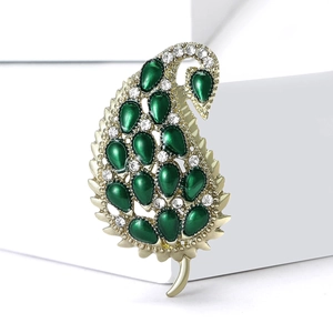 Elegant gold peacock leaf brooch with green enamel and sparkling crystals on white pedestal