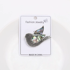 Detailed close-up of a silver pigeon brooch with iridescent abalone shell inlay details