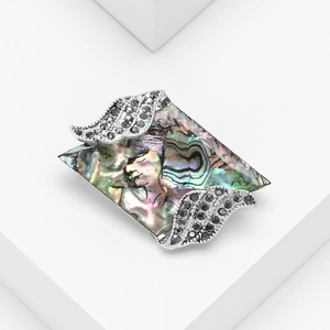 Parallelogram brooch with abalone shell and black crystal wing design on a white pedestal