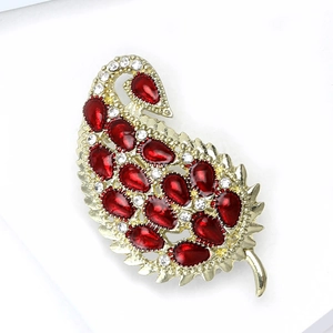 Detail view of a golden alloy feather brooch featuring red water-drop gems and rhinestones