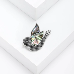 Elegant silver pigeon brooch with iridescent abalone shell wings on a white pedestal