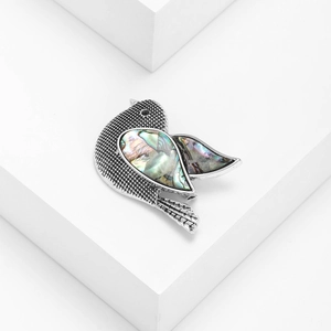 Elegant silver bird brooch featuring colorful abalone shell inlays on a white pedestal
