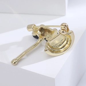Detailed close-up of the golden auction gavel brooch showing the pin mechanism and enamel