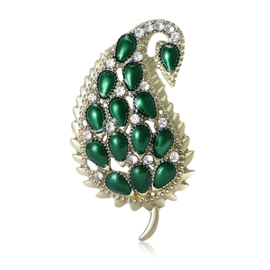 Elegant gold leaf brooch with green gemstones and crystal accents on a white background