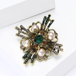 Macro detail of Baroque brooch with emerald crystal and cream pearls in gold finish