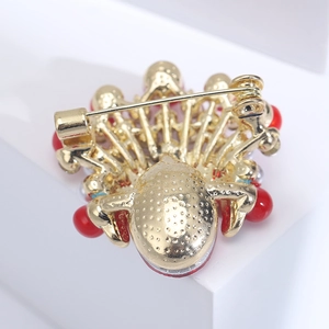 Detail view showing golden metal alloy back with safety pin clasp and red bead edges